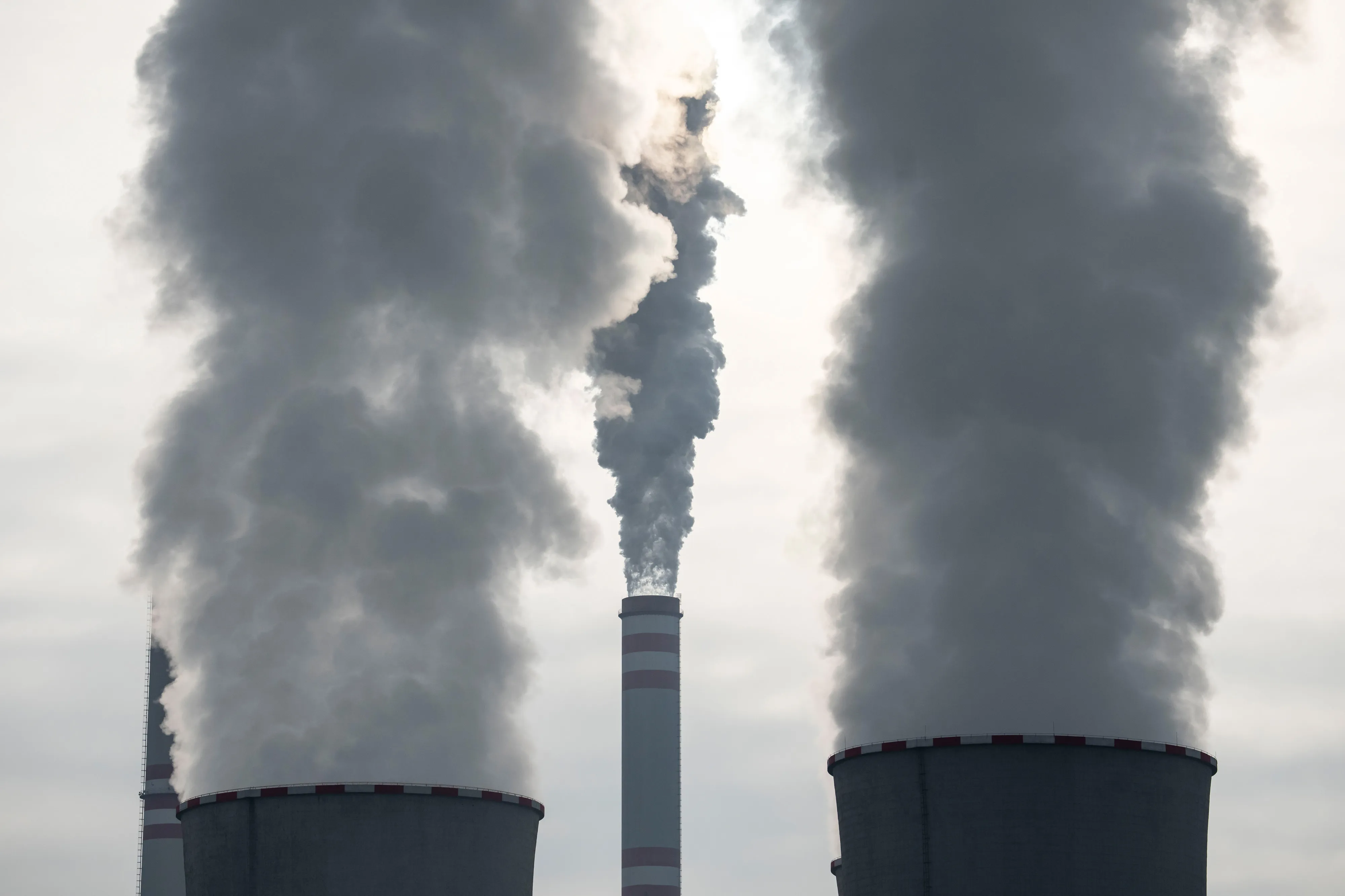 Large plumes rise above industrial cooling towers and chimneys